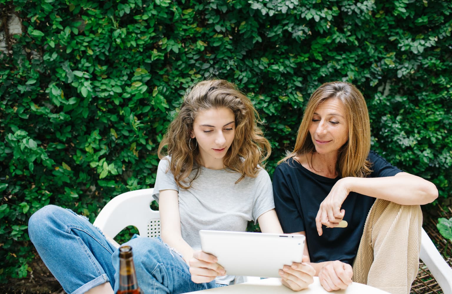 2 Freundinnen sitzen im Garten und schauen auf das Tablet - Rechnung per Post auch möglich