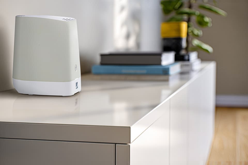 Weißer Router auf weißem Sideboard mit Büchern und Zimmerpflanze im Hintergrund in modernem Wohnraum.