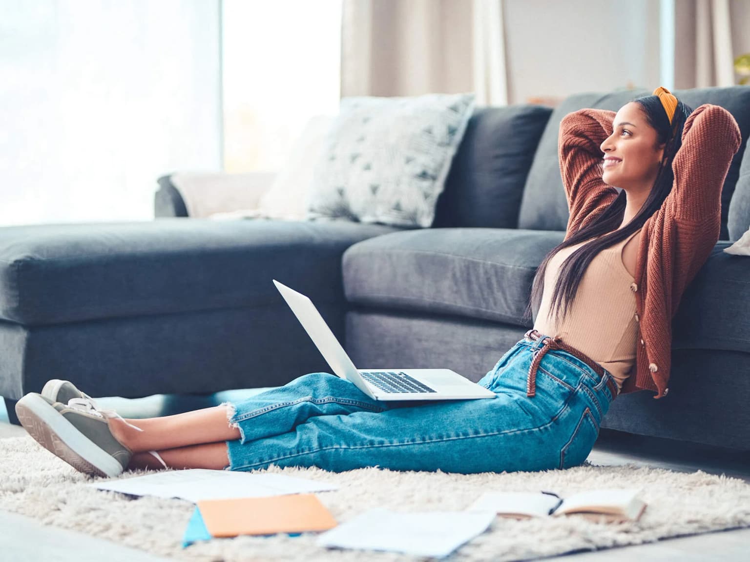Frau sitzt auf dem Boden mit dem laptop auf dem Schoß und verschärnkt die Arme hinter dem Kopf