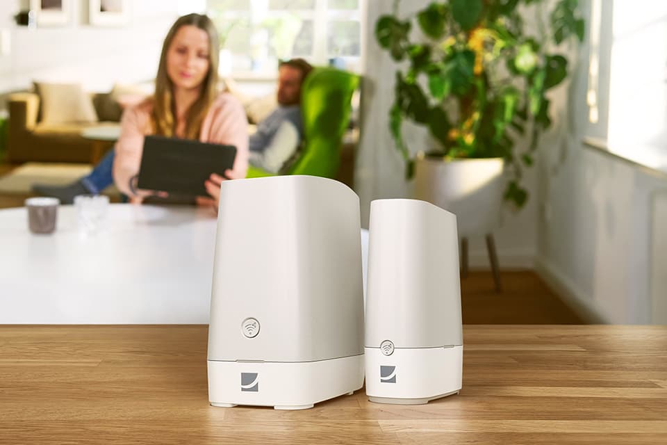 Frau und Mann sitzen im Wohnzimmer auf der Couch und bedienen das Tablet für die DG WLAN Plus Bundle Router