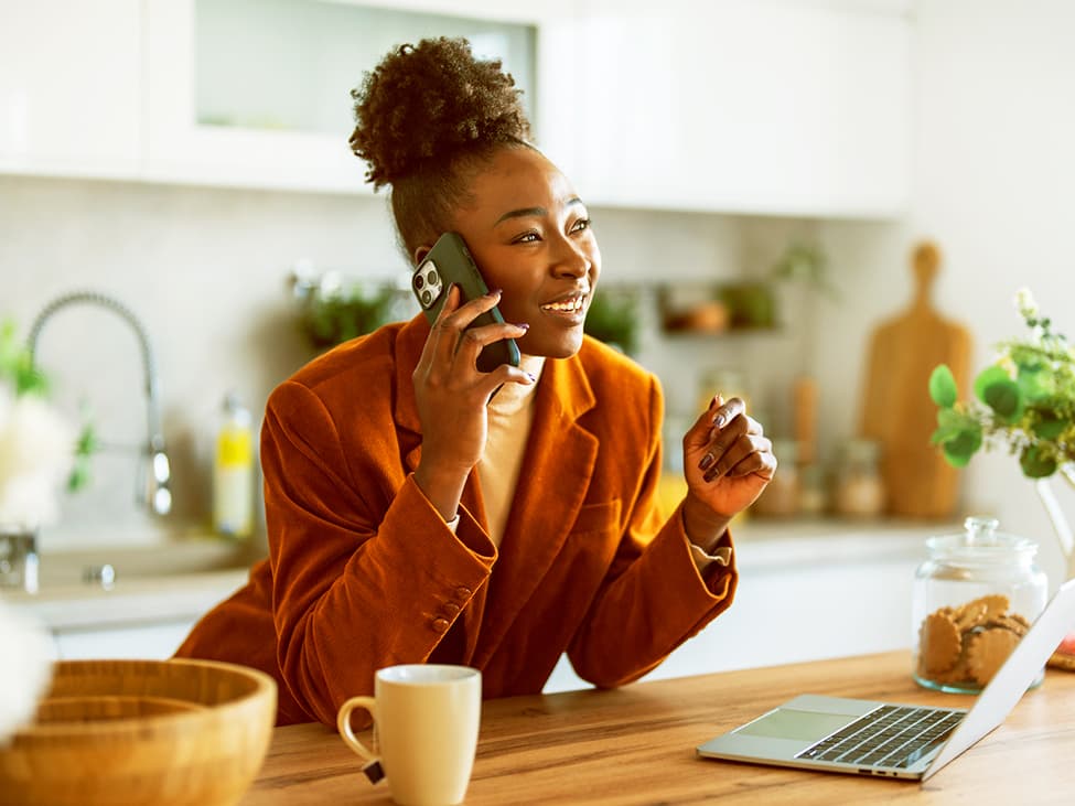 Frau in orangenen Blazer telefoniert mit dem Handy lächelnd in der Küche