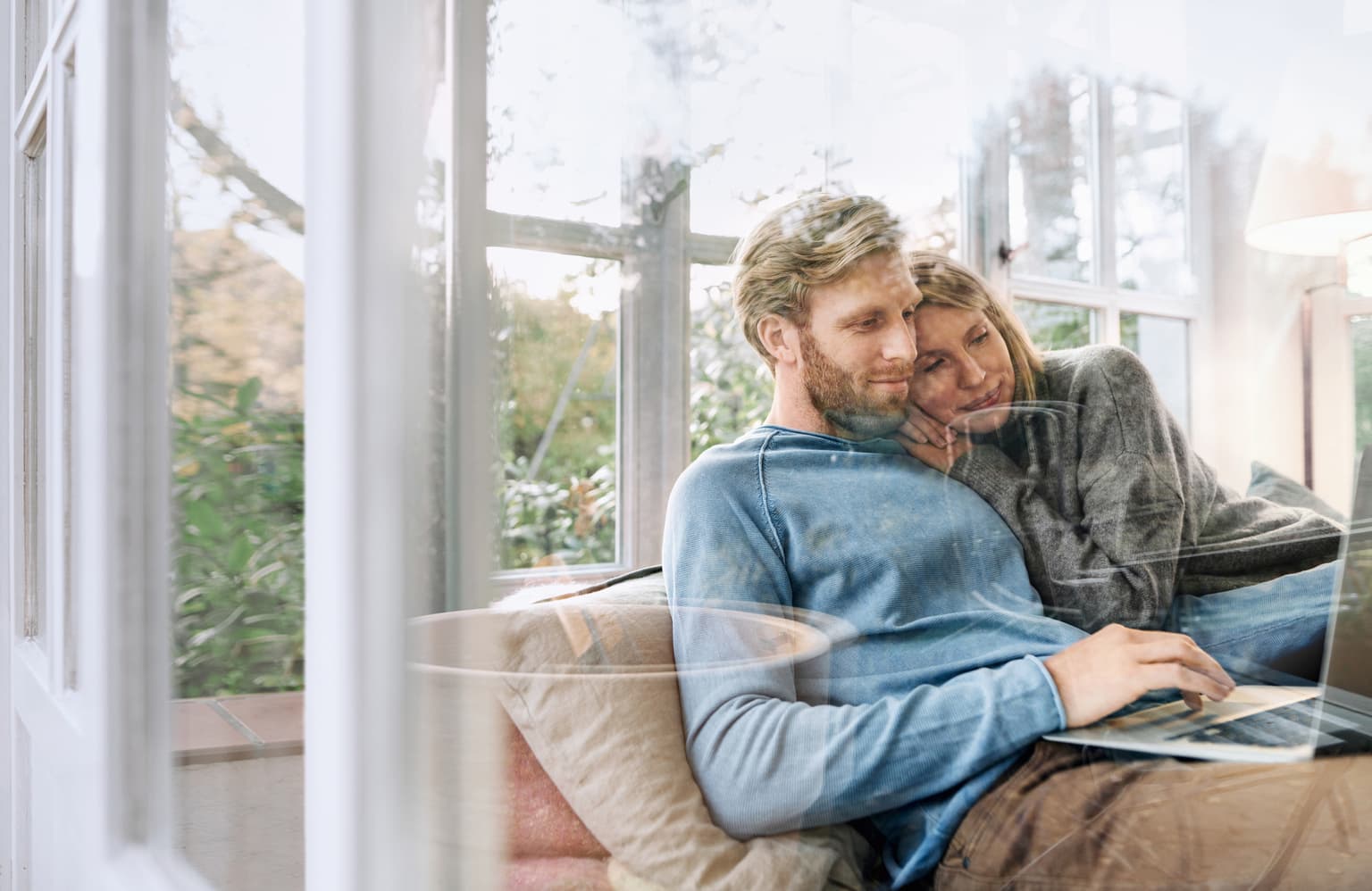 Frau und Mann kuscheln auf dem Sofa und schauen auf ein Laptop