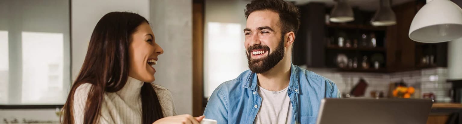 Wohnungswirtschaft Frau und Mann sitzen am Küchentisch mit Laptop und lächeln sich an