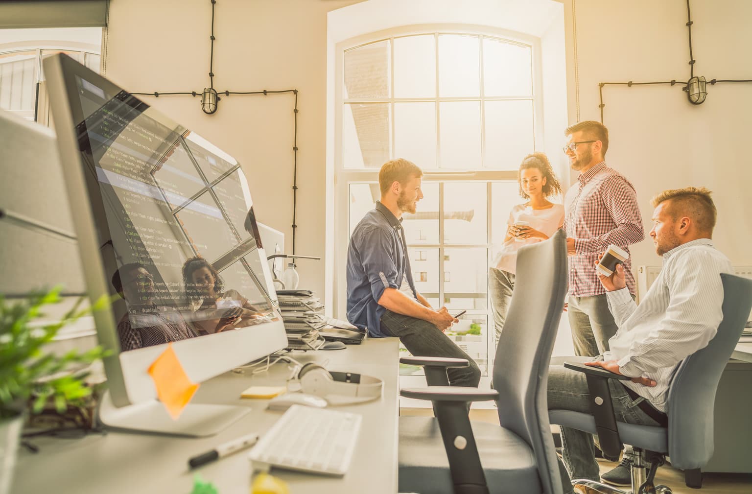 B2B Vernetzung & Outsourcing - Team sitzt im Büro und unterhält sich, während die Sonne durch das große Fenster scheint