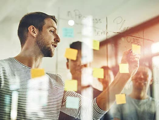 Büro Team plant ein Meeting mit Notiz Zettel an einer Glas Wand
