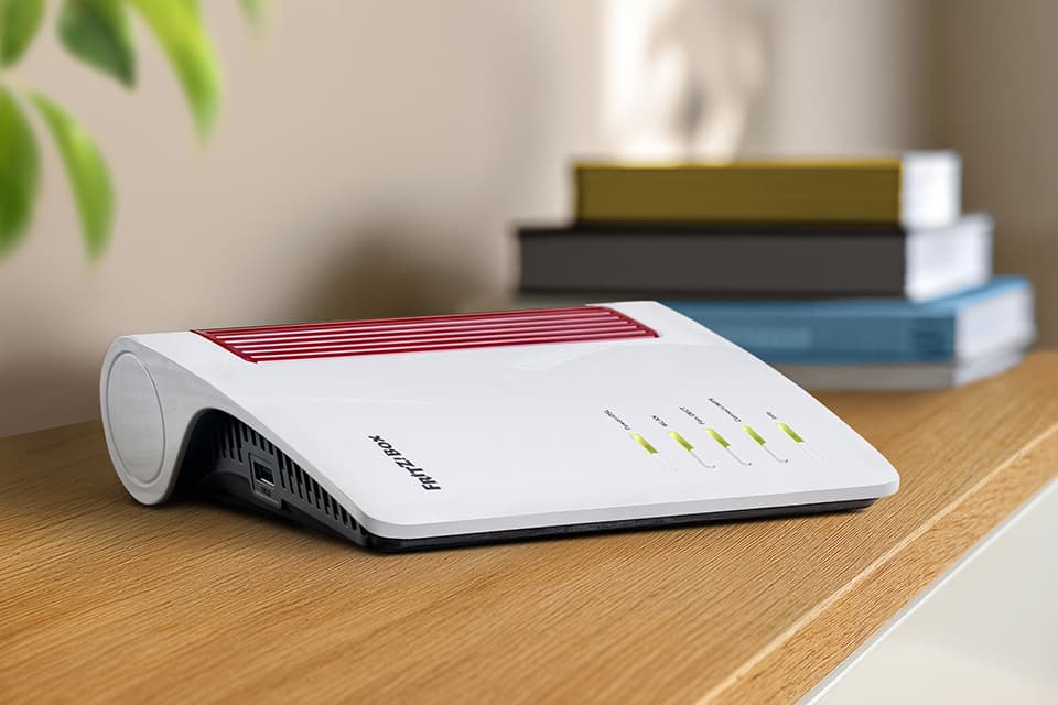 Weißer FRITZ!Box-Router auf Holztisch, gestapelte Bücher im Hintergrund.