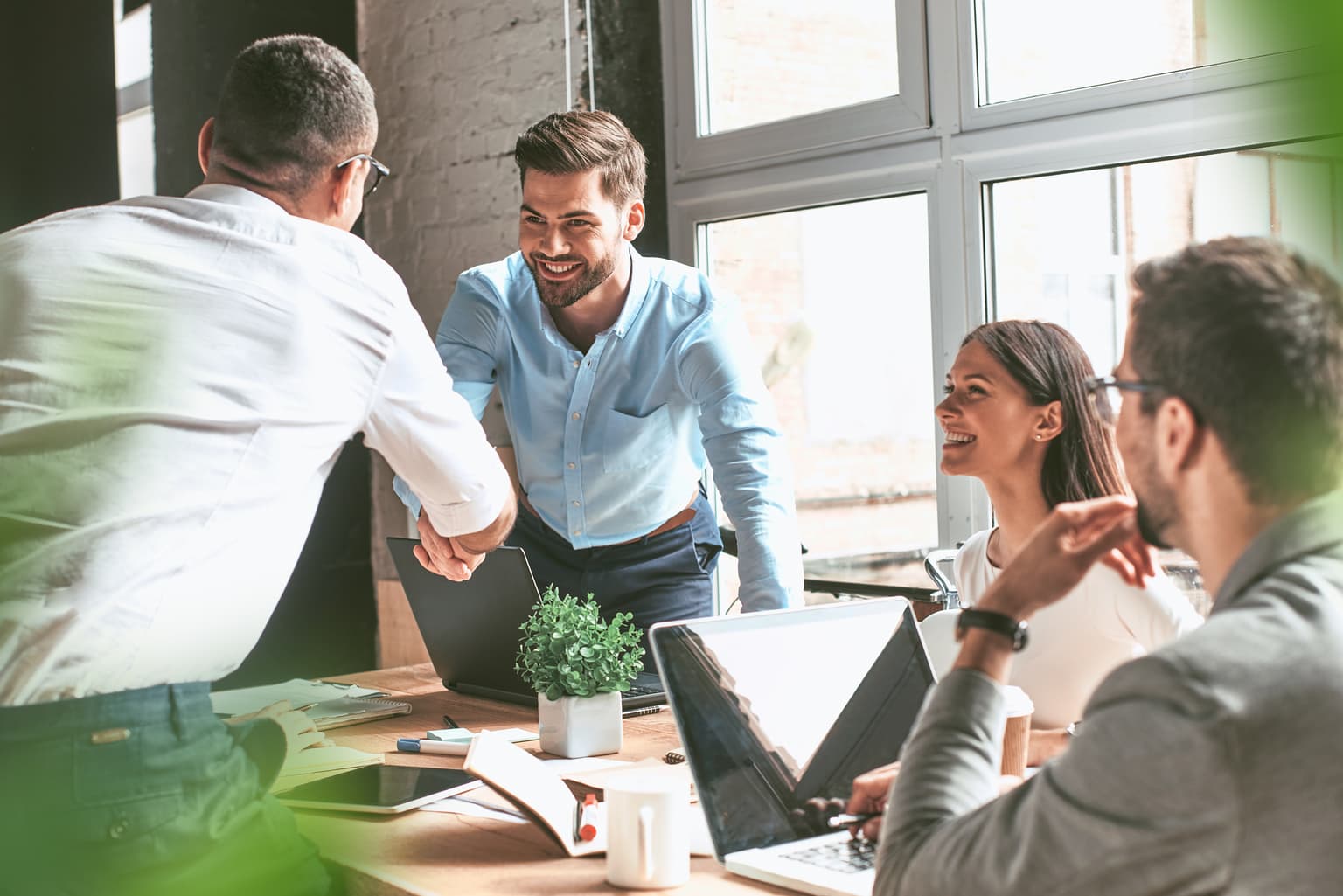 Team sitzt im Büro und begrüßt den Kunden. Die Personen geben sich die Hand. Referenzen B2B Kunden