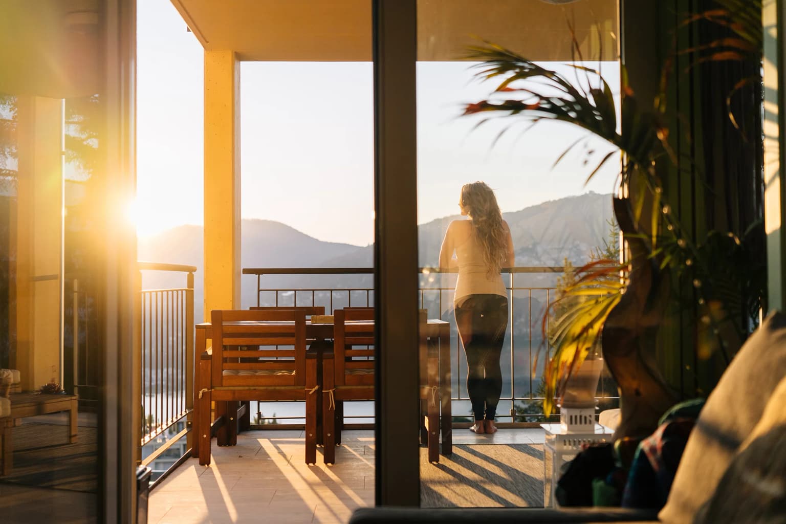 Eine Frau steht im Sonnenuntergang auf ihrer Terasse und schaut in die Ferne