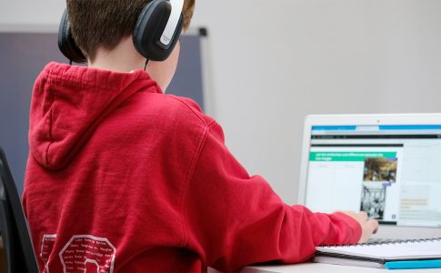 Junge mit rotem Pullover und Kopfhörern sitzt vor einem Laptop