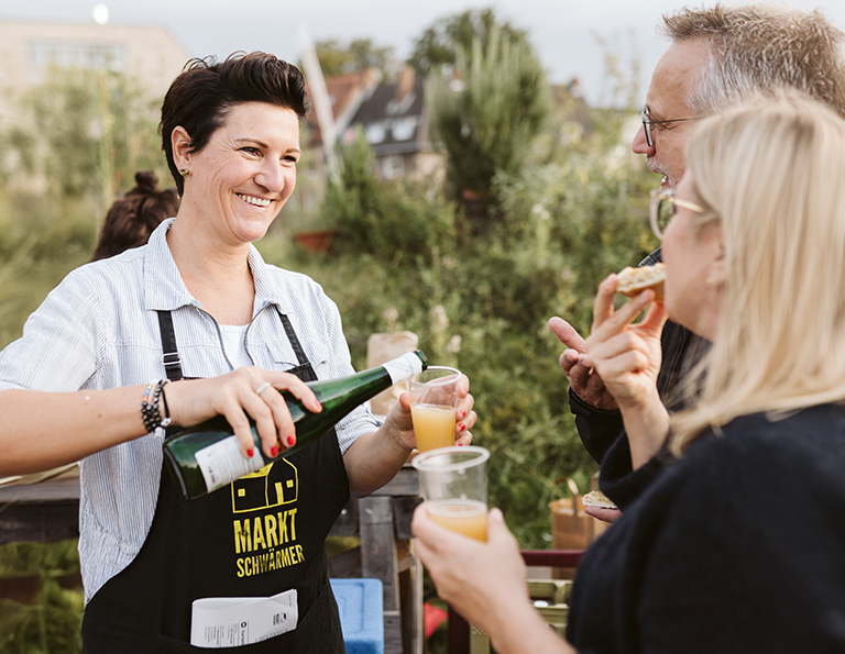 Eine Frau schenkt zwei Gästen zwei Saft zum Probieren aus.