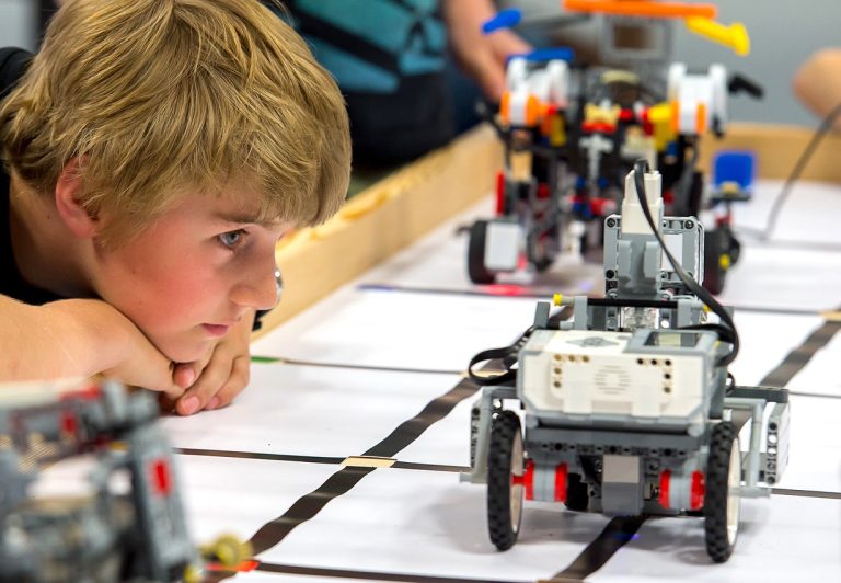 Ein Junge beobachtet ein Lego-Roboter-Fahrzeug, das auf einem Tisch fährt.