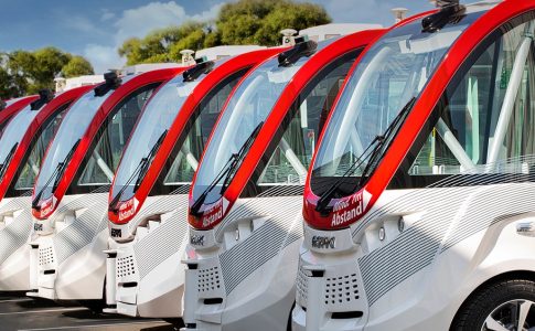 Sechs weiße Kleinbusse mit roten Streifen stehen nebeneinander.