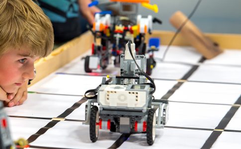 Ein Junge beobachtet ein Lego-Roboter-Fahrzeug, das auf einem Tisch fährt.